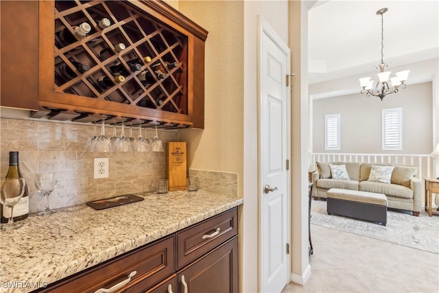 bar featuring light stone countertops, decorative backsplash, light tile patterned flooring, decorative light fixtures, and a chandelier