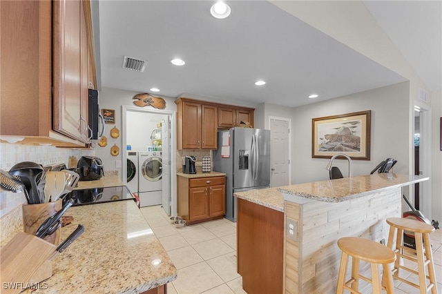 kitchen featuring decorative backsplash, independent washer and dryer, light stone counters, stainless steel fridge with ice dispenser, and a breakfast bar area