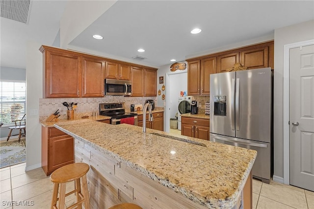 kitchen featuring light stone counters, a kitchen bar, a kitchen island with sink, light tile patterned floors, and appliances with stainless steel finishes