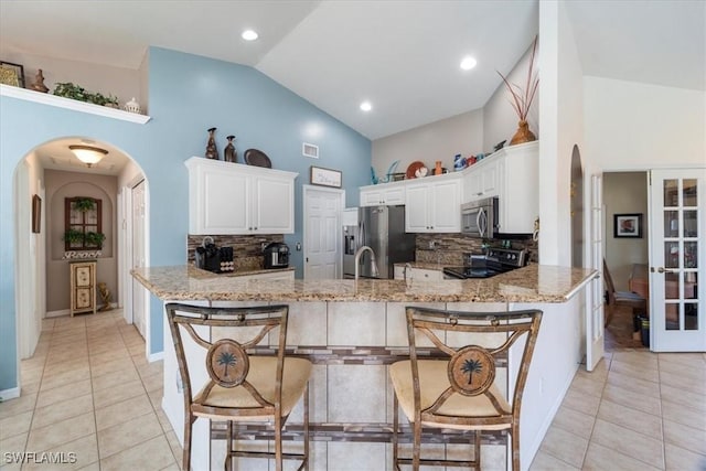 kitchen featuring white cabinets, a kitchen bar, light stone counters, kitchen peninsula, and stainless steel appliances