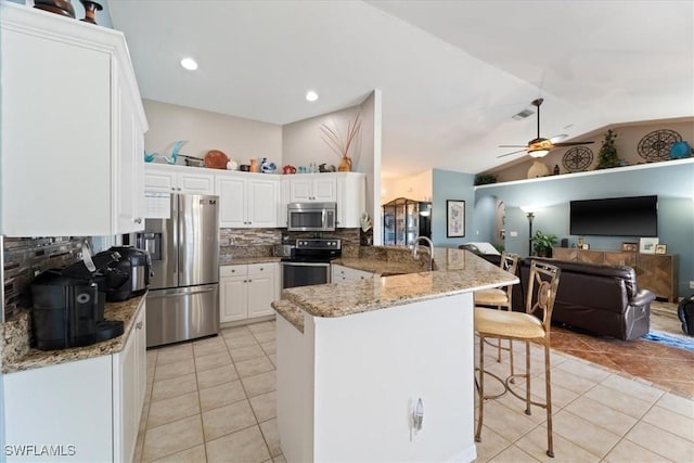 kitchen featuring appliances with stainless steel finishes, a breakfast bar, stone counters, white cabinetry, and lofted ceiling