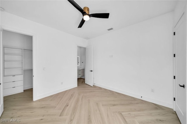 unfurnished bedroom featuring ceiling fan, a closet, a walk in closet, and light parquet flooring