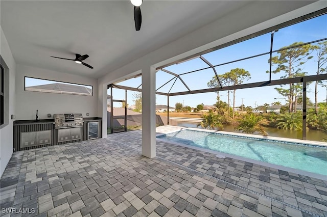 view of pool featuring glass enclosure, sink, exterior kitchen, a patio area, and a water view