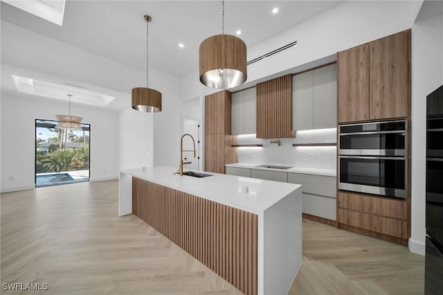 kitchen with white cabinets, sink, hanging light fixtures, an island with sink, and double oven