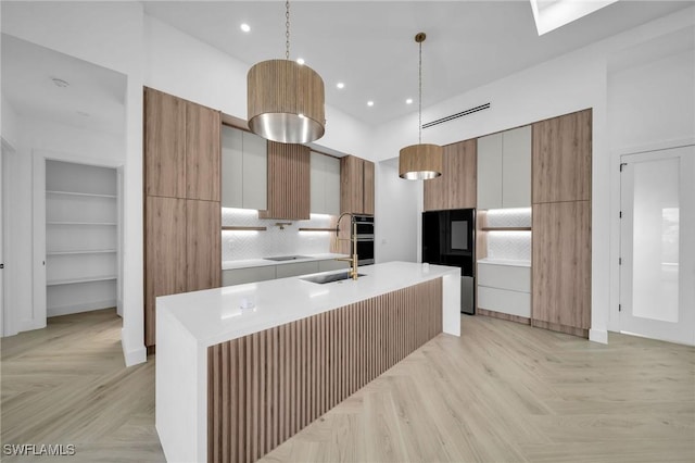 kitchen featuring a center island with sink, light parquet flooring, hanging light fixtures, and sink