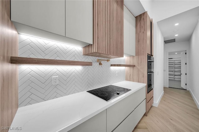 kitchen with white cabinets, black electric cooktop, double oven, tasteful backsplash, and light hardwood / wood-style floors