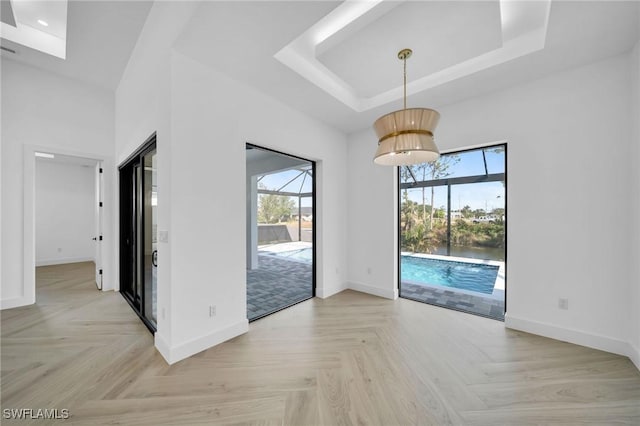 interior space with a tray ceiling, light parquet floors, and a healthy amount of sunlight