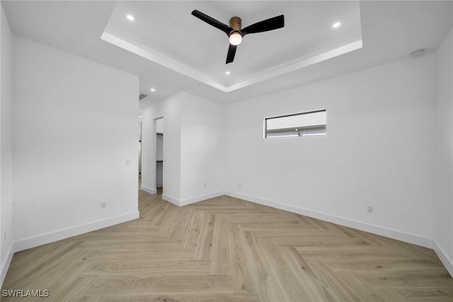 empty room featuring a tray ceiling, ceiling fan, and light parquet flooring