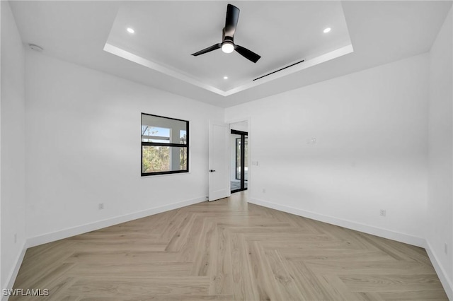 unfurnished room with a raised ceiling, ceiling fan, and light parquet floors