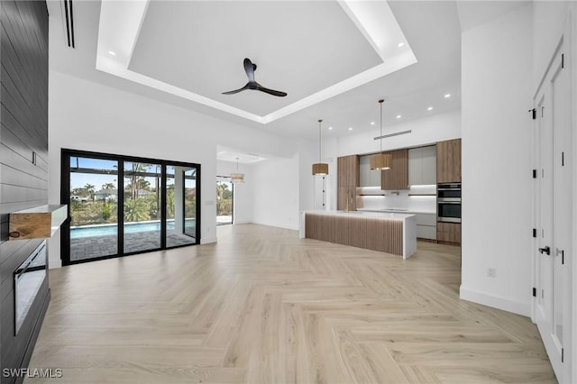 unfurnished living room featuring a towering ceiling, a tray ceiling, light parquet floors, and ceiling fan