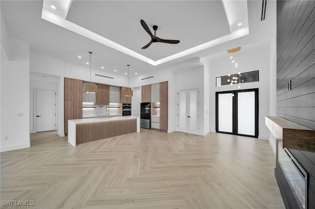 unfurnished living room featuring light parquet floors, ceiling fan with notable chandelier, sink, a towering ceiling, and a tray ceiling