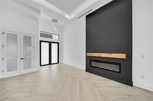 unfurnished living room featuring french doors, a large fireplace, and light parquet flooring