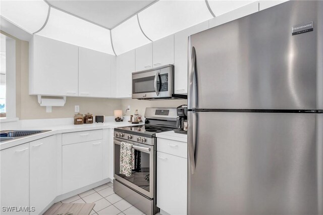 kitchen with sink, white cabinets, light tile patterned flooring, and appliances with stainless steel finishes