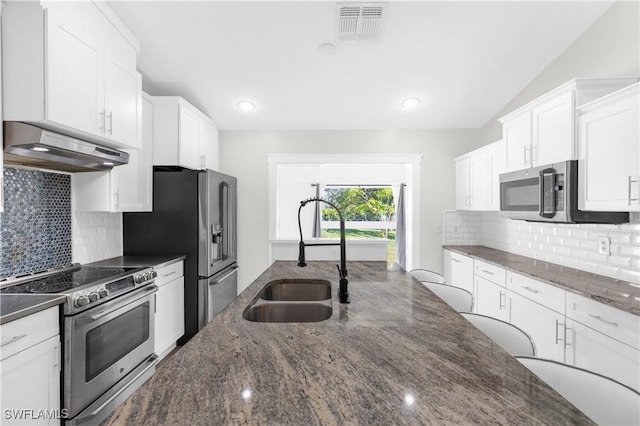 kitchen featuring appliances with stainless steel finishes, sink, dark stone countertops, white cabinets, and lofted ceiling