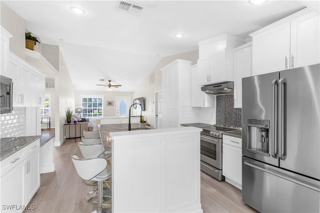 kitchen with appliances with stainless steel finishes, backsplash, vaulted ceiling, white cabinets, and a center island