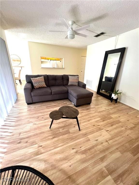 living room with ceiling fan, a textured ceiling, and light wood-type flooring