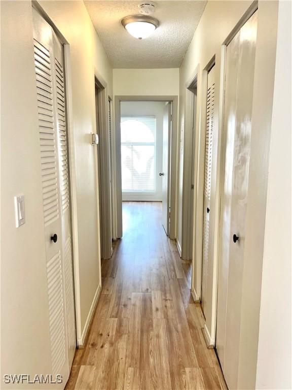 corridor with light hardwood / wood-style floors and a textured ceiling