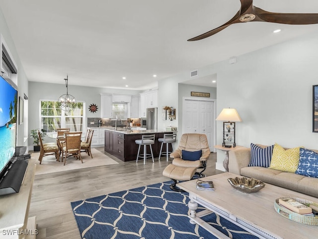 living room featuring light hardwood / wood-style flooring, ceiling fan with notable chandelier, and sink