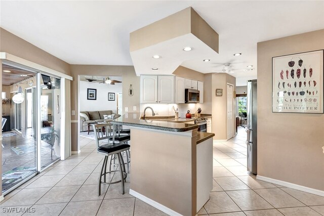 kitchen featuring kitchen peninsula, appliances with stainless steel finishes, light tile patterned floors, white cabinets, and a breakfast bar area