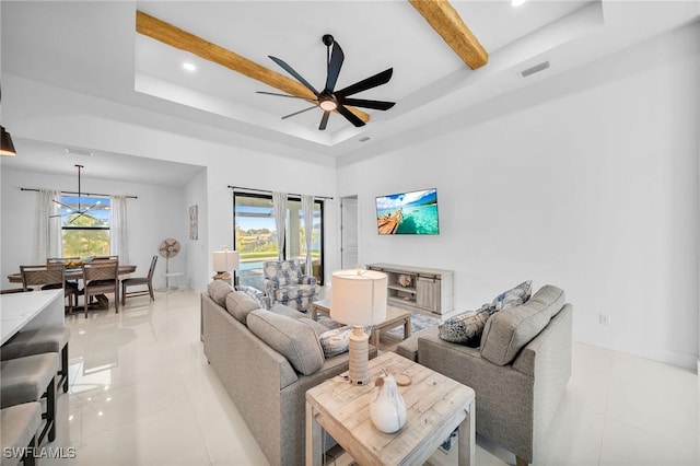 tiled living room with beam ceiling, ceiling fan with notable chandelier, and a raised ceiling