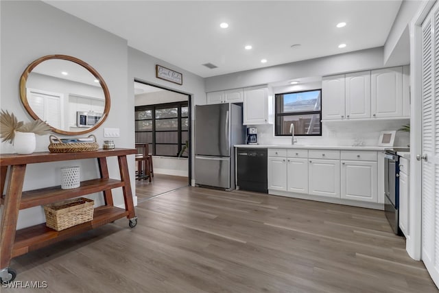 kitchen featuring appliances with stainless steel finishes, tasteful backsplash, sink, white cabinets, and hardwood / wood-style floors