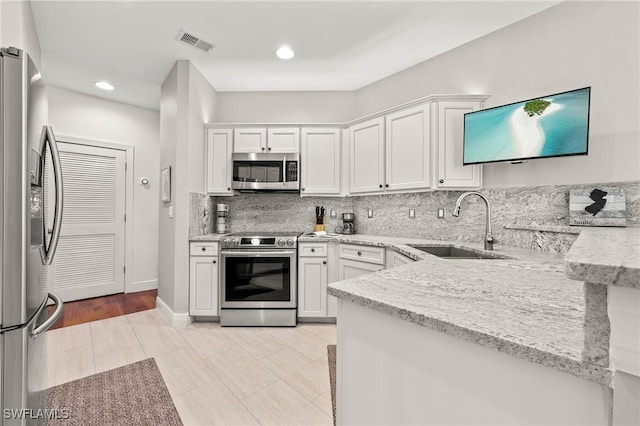 kitchen featuring light stone countertops, appliances with stainless steel finishes, backsplash, sink, and white cabinetry