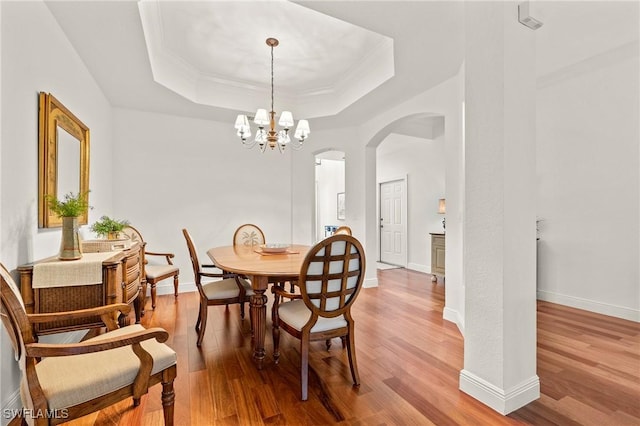 dining area with a raised ceiling, light hardwood / wood-style flooring, and an inviting chandelier