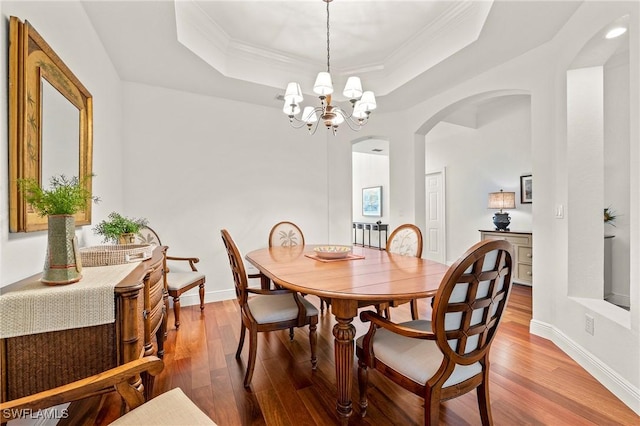 dining room featuring a tray ceiling, crown molding, wood-type flooring, and a notable chandelier