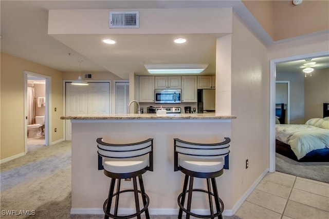 kitchen featuring light stone counters, a breakfast bar area, visible vents, appliances with stainless steel finishes, and light carpet