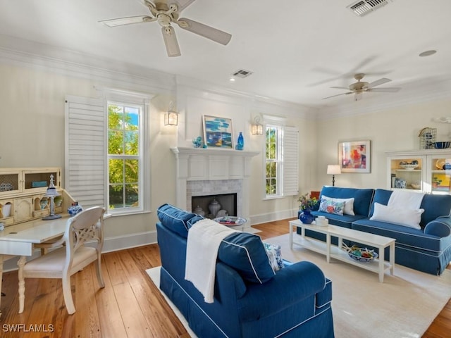 living room with a tile fireplace, light hardwood / wood-style flooring, ceiling fan, and crown molding