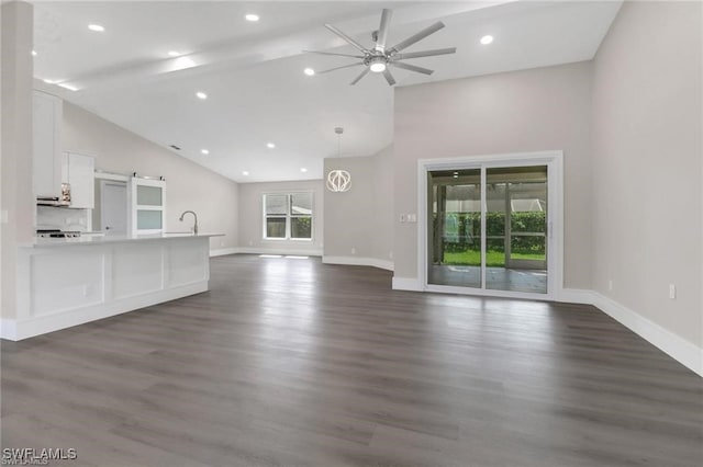 unfurnished living room with dark wood-type flooring, high vaulted ceiling, sink, ceiling fan, and a barn door