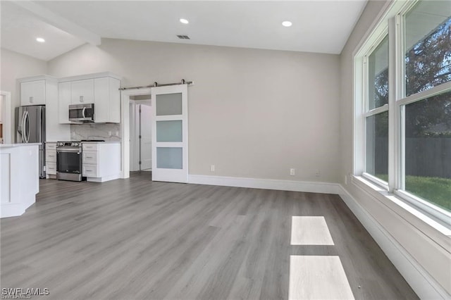 kitchen with appliances with stainless steel finishes, a barn door, light hardwood / wood-style flooring, white cabinets, and vaulted ceiling with beams