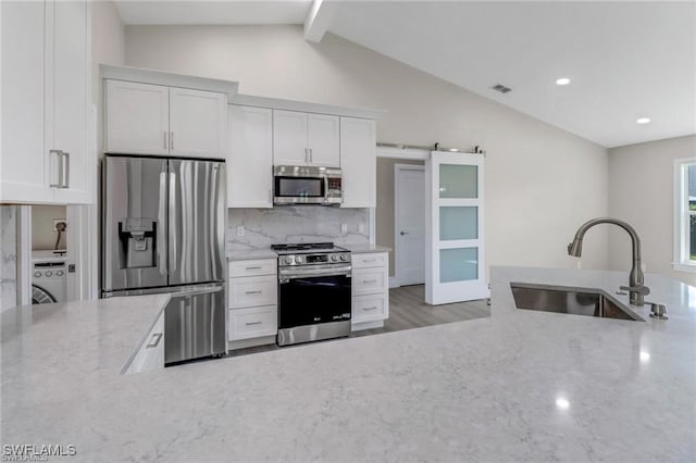 kitchen featuring sink, vaulted ceiling with beams, light stone countertops, white cabinetry, and stainless steel appliances