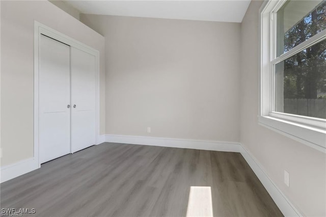 unfurnished bedroom featuring hardwood / wood-style floors, a closet, and multiple windows