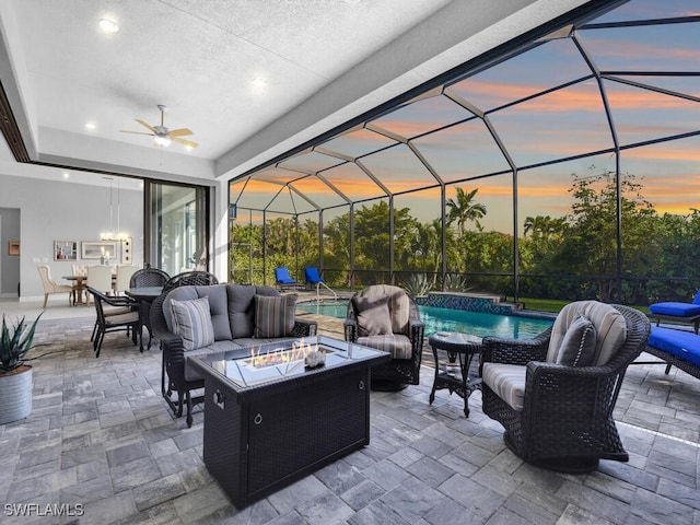 patio terrace at dusk featuring pool water feature, ceiling fan, a lanai, and an outdoor living space with a fire pit