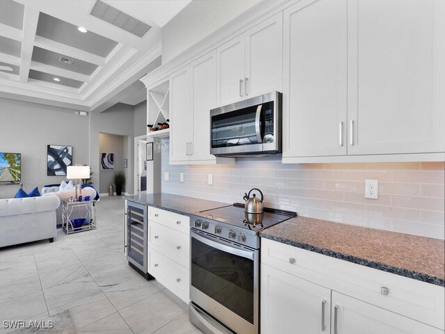 kitchen featuring appliances with stainless steel finishes, backsplash, beverage cooler, beamed ceiling, and white cabinetry