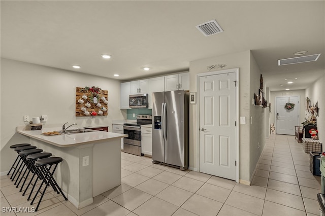 kitchen with light tile patterned floors, kitchen peninsula, a kitchen bar, white cabinets, and appliances with stainless steel finishes