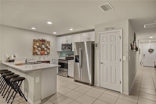 kitchen featuring kitchen peninsula, light tile patterned floors, appliances with stainless steel finishes, a kitchen bar, and white cabinetry