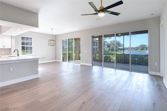 unfurnished living room with ceiling fan with notable chandelier, sink, and light hardwood / wood-style flooring