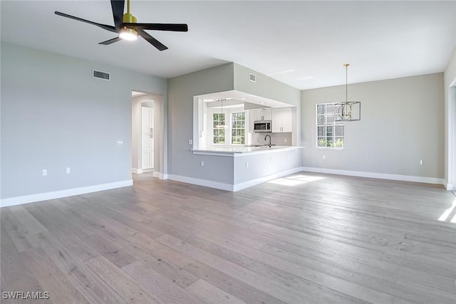 unfurnished living room featuring light wood-type flooring, ceiling fan with notable chandelier, and sink