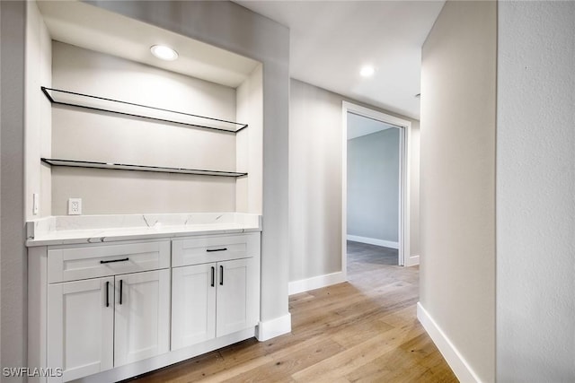 bar featuring light stone countertops, light hardwood / wood-style flooring, and white cabinetry