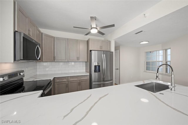 kitchen with tasteful backsplash, light stone counters, stainless steel appliances, ceiling fan, and sink