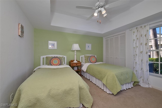 carpeted bedroom with a tray ceiling, ceiling fan, and a closet