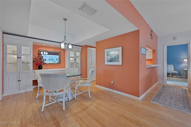 dining space with a tray ceiling, light hardwood / wood-style floors, and an inviting chandelier