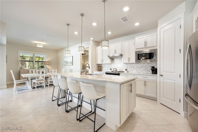 kitchen with white cabinets, an island with sink, stainless steel appliances, and decorative light fixtures