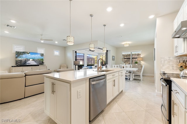 kitchen with appliances with stainless steel finishes, a kitchen island with sink, sink, white cabinetry, and hanging light fixtures