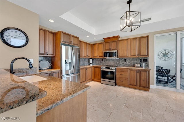 kitchen with light stone countertops, tasteful backsplash, stainless steel appliances, sink, and hanging light fixtures