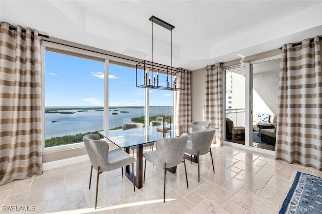 dining room featuring a chandelier, a water view, and a raised ceiling