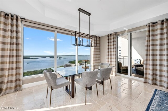 dining space featuring stone tile floors, baseboards, an inviting chandelier, a tray ceiling, and a water view