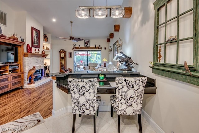 dining space with light tile patterned floors, a stone fireplace, and ceiling fan